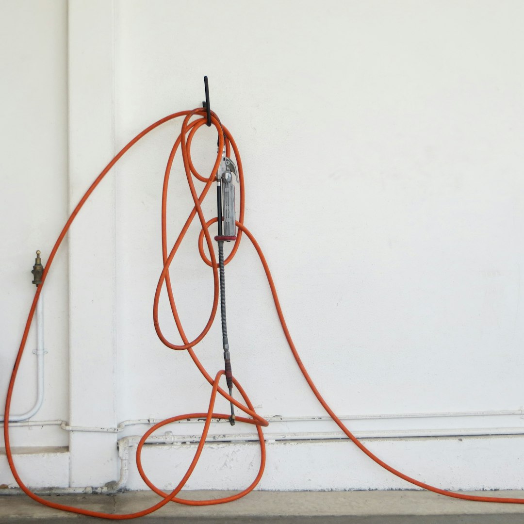 Összekötött és feltekert narancssárga elektromos kábel fekete csatlakozóval a fehér falon